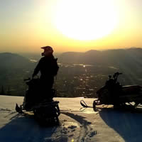 A sledder is silhouetted against the setting sun looking over an amazing panorama of the town below. 