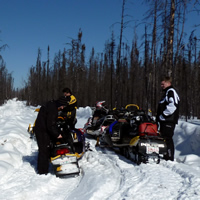 A group of sledders take a break on a cutline trail surrounded by bush.