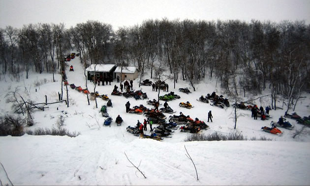A large group of sleds gather around a cabin, seen from above. 