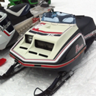 A vintage black, white and red Polaris snowmobile is parked next to a new black, white and red polaris snowmobile.