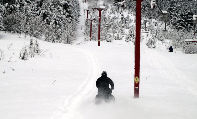 A sledder rides down the powder alongside a defunct ski lift.