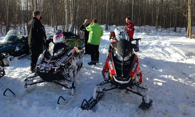 A group of riders pause with their sleds in a cabin next to forest.