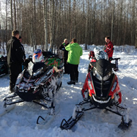 A group of riders pause with their sleds in a cabin next to forest.