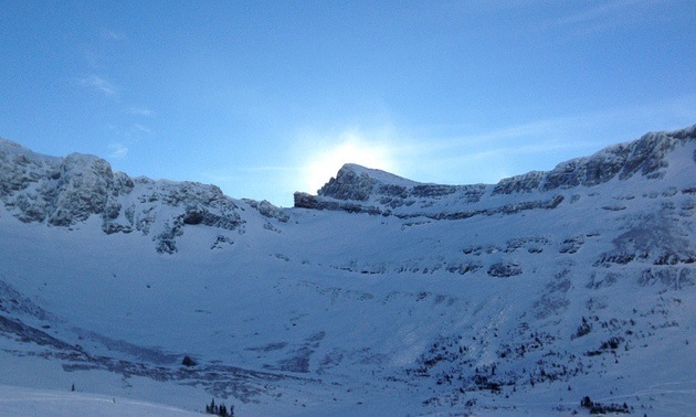 A photo of the sun going behind a snow filled mountian bowl in the Crowsnest Pass. 