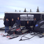People standing near two snowmobiles and a large trailer