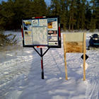 snowmobiles next to some information signs out on a snowy trail
