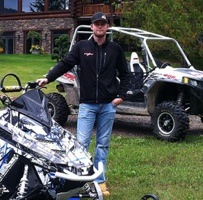 Nick Bredt standing beside his snowmobile and  side x side. 