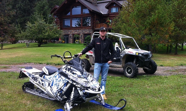 Nick Bredt standing beside his snowmobile and  side x side. 