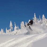 A snowmobiler getting some air on a perfectly clear day.