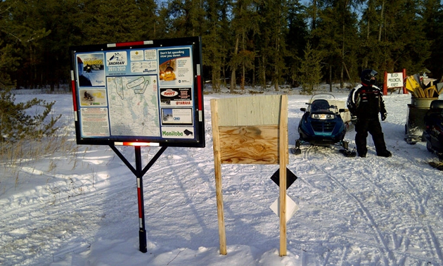 snowmobiles next to some information signs out on a snowy trail
