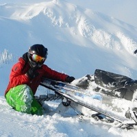Curtis Pawliuk sitting next to his sled, enjoying the blue sky and deep powder in Valemount BC. 
