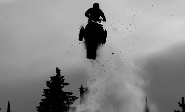 A black and white photo of a snowmobiler in the air. 