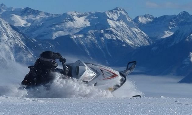 A snowmobiler laying it over with the mountains in the background. 