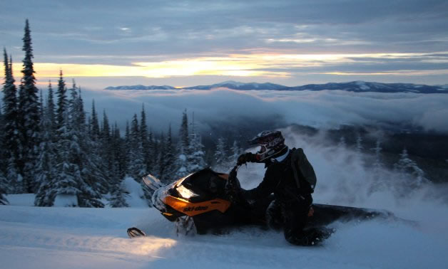 A snowmobiler carving with the setting sun in the background. 