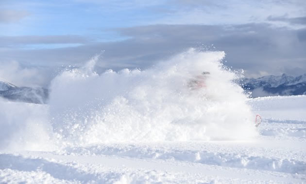 A snowmobiler spraying up a huge cloud of snow around him. 