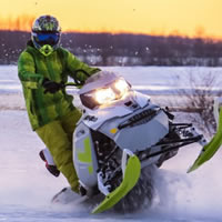 A rider in a green snowmobile suit on a green and white snowmobile. 