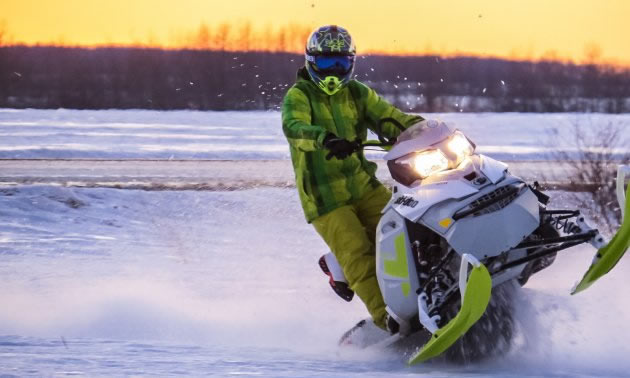 A rider in a green snowmobile suit on a green and white snowmobile. 