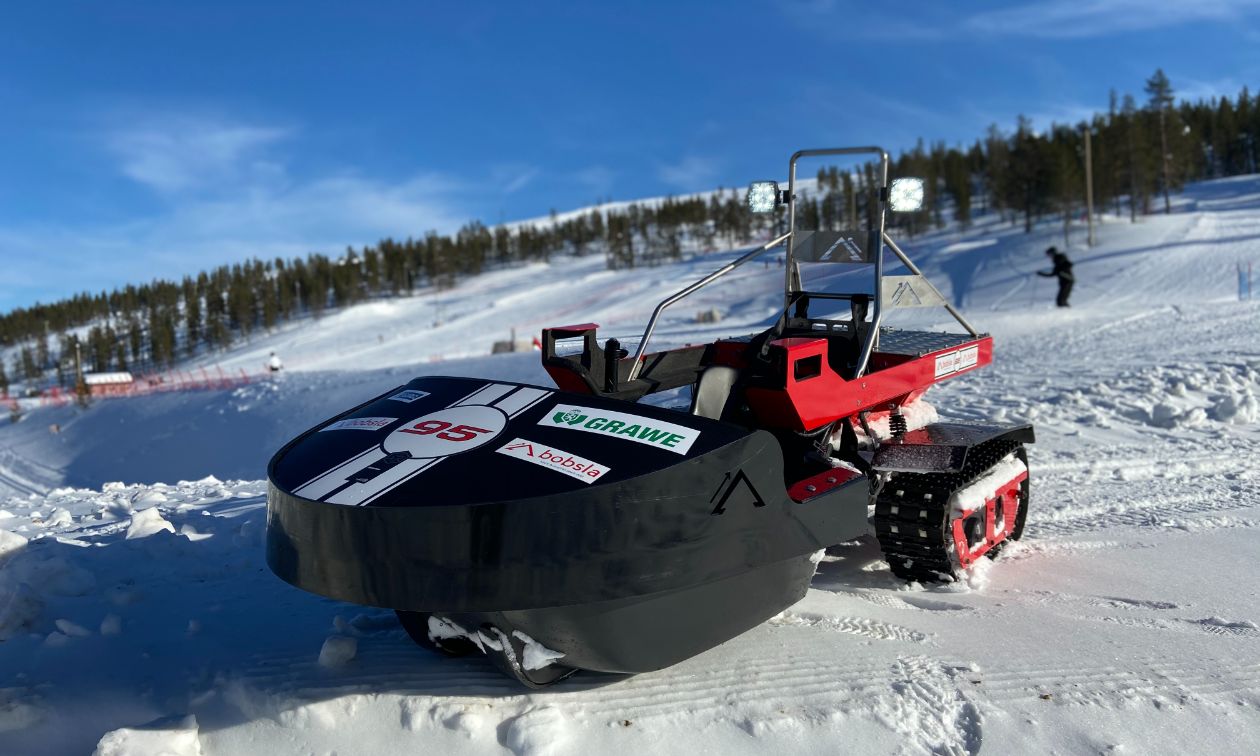 A black Bobsla electric snowmobile is parked on snow. 