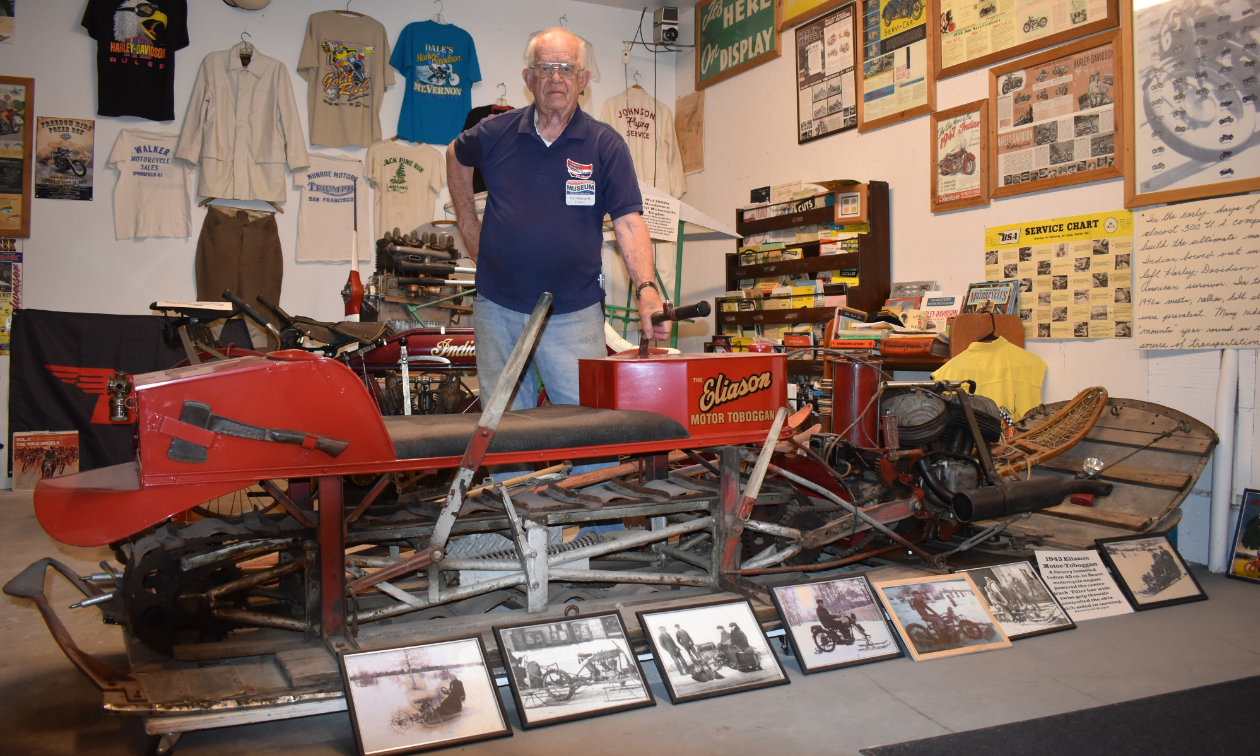 Gil Mangels stands behind a red 1943 Eliason Snow Toboggan. 