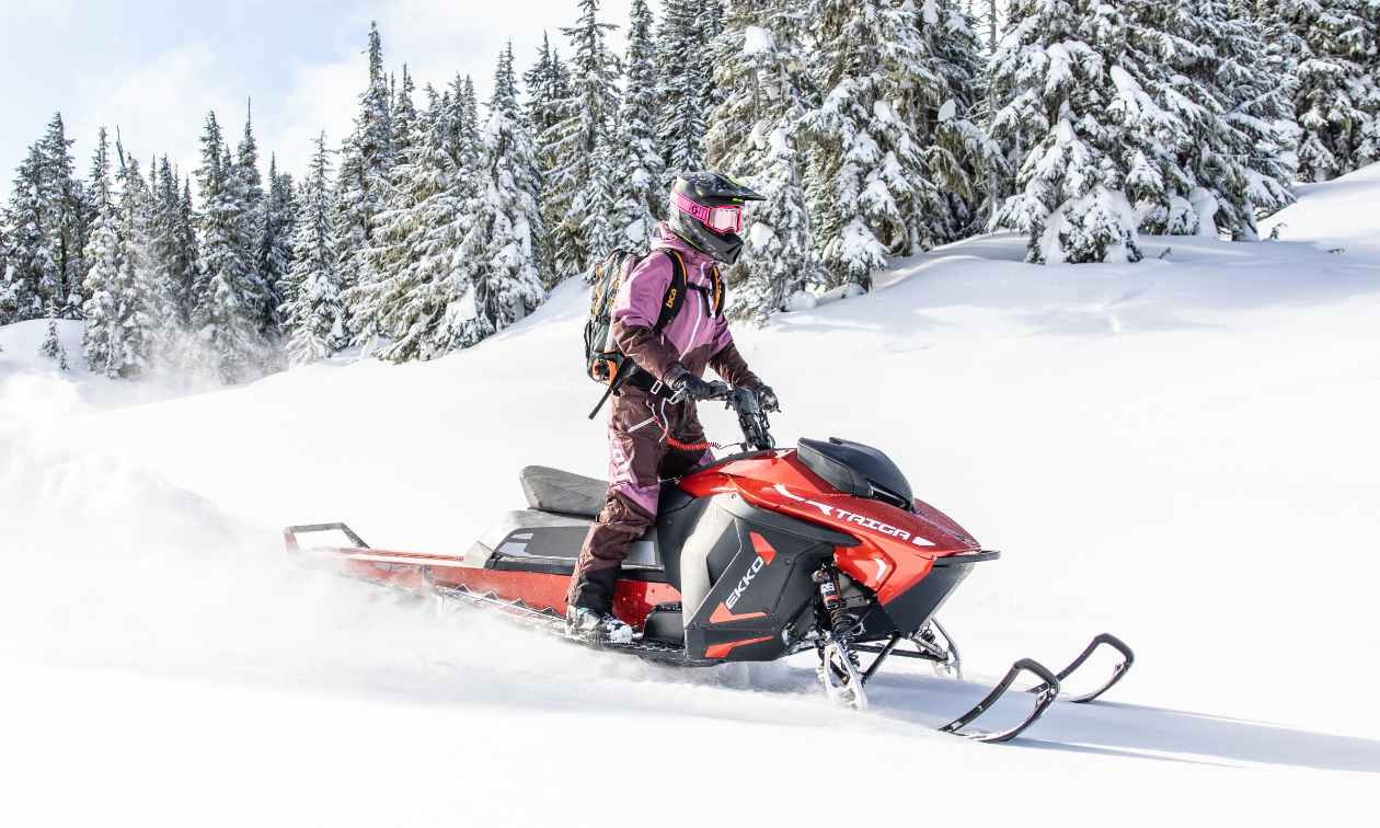 A snowmobiler in a pink jacket rides a red Taiga snowmobile. 