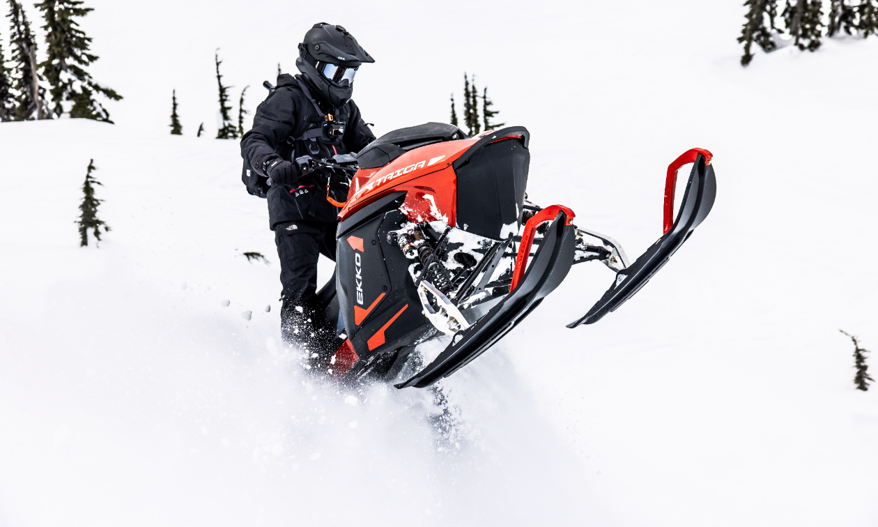 A snowmobiler wearing all black does a wheelie with a snowmobile. 