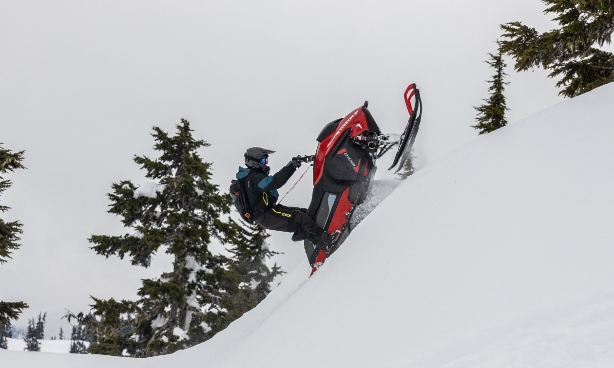 A snowmobiler rides up a mountain on a red Taiga snowmobile. 