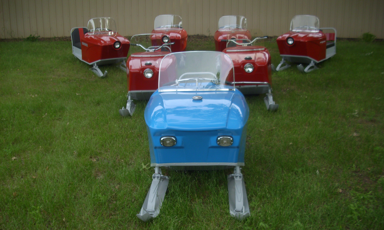 A blue Sno Scoot in front of six red Sno Scoot snowmobiles.