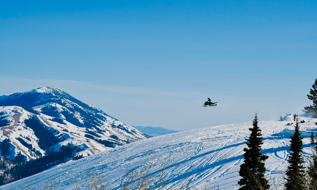 A wide shot on a mountain with Alonzo Coby flying through the air on his snowmobile.