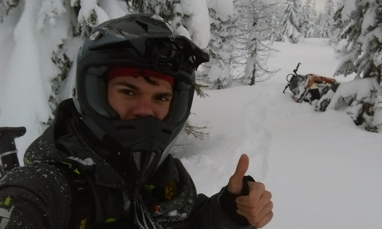 Andrew McKenzie wears a black jacket and helmet, giving a thumbs up in a snowy forest.