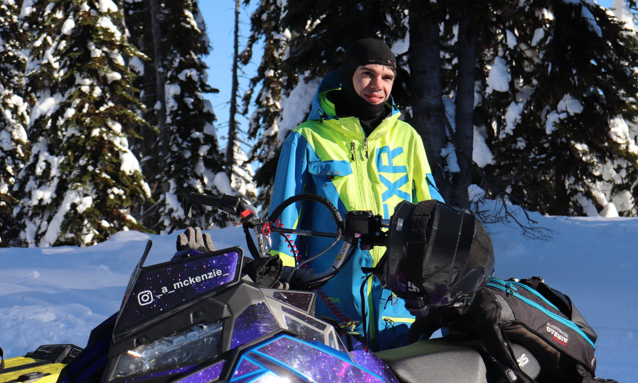 Andrew McKenzie wears a bright green and blue jacket in a sunny forest.