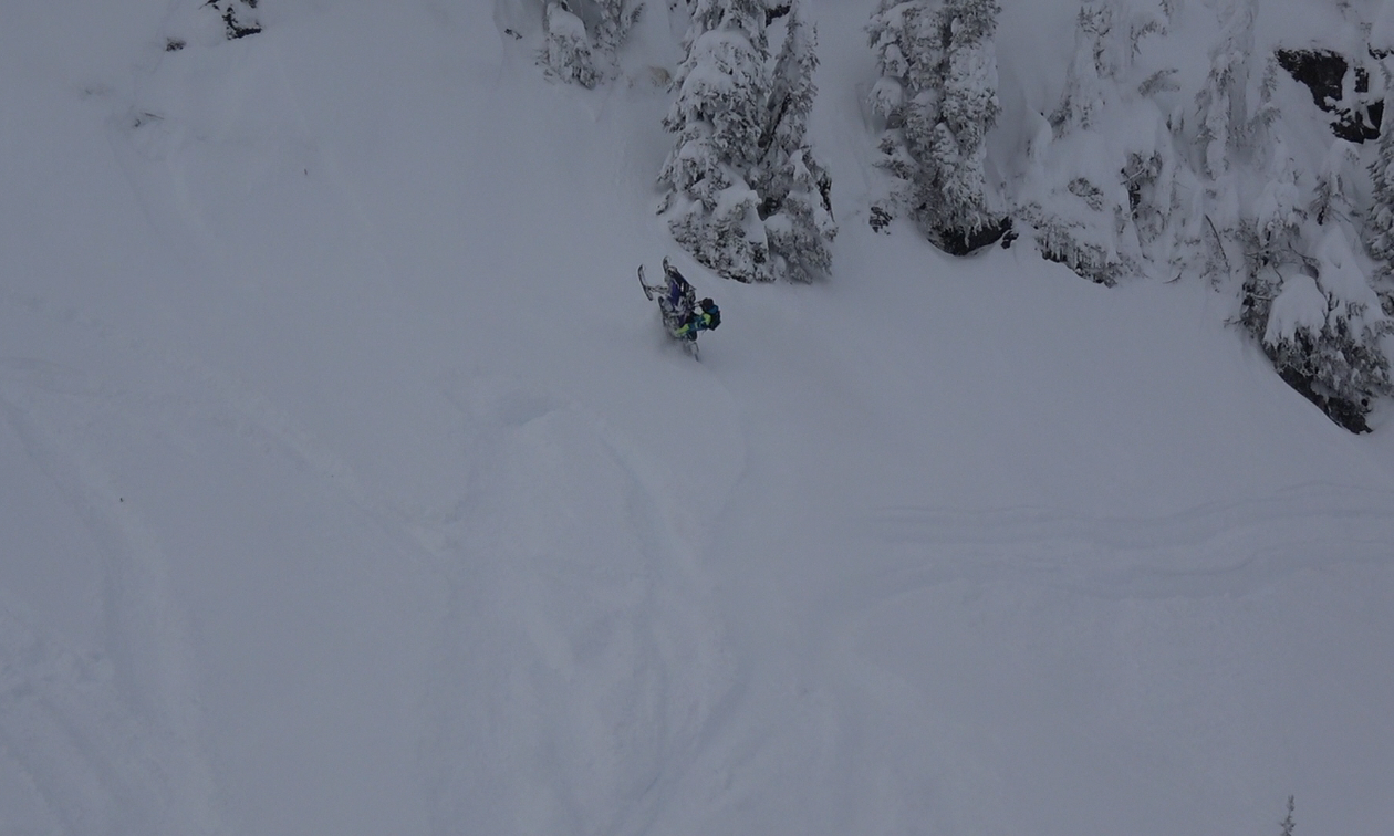 A snowmobiler hill climbs up a steep embankment. 