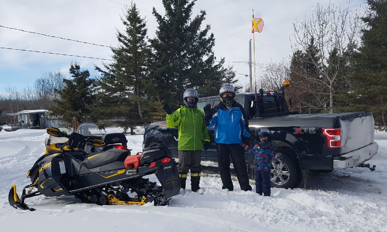 Audun Klath stands next to his father, son and a truck and two snowmobiles. 