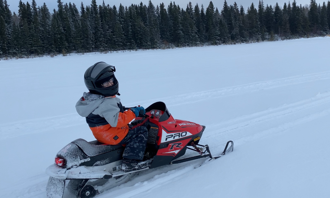 Audun Klath’s son rides a small snowmobile on a prairie field. 