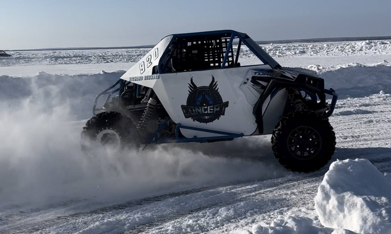 A Polaris RZR slides across a corner on a snowy race track, spraying powdery snow in the process. 