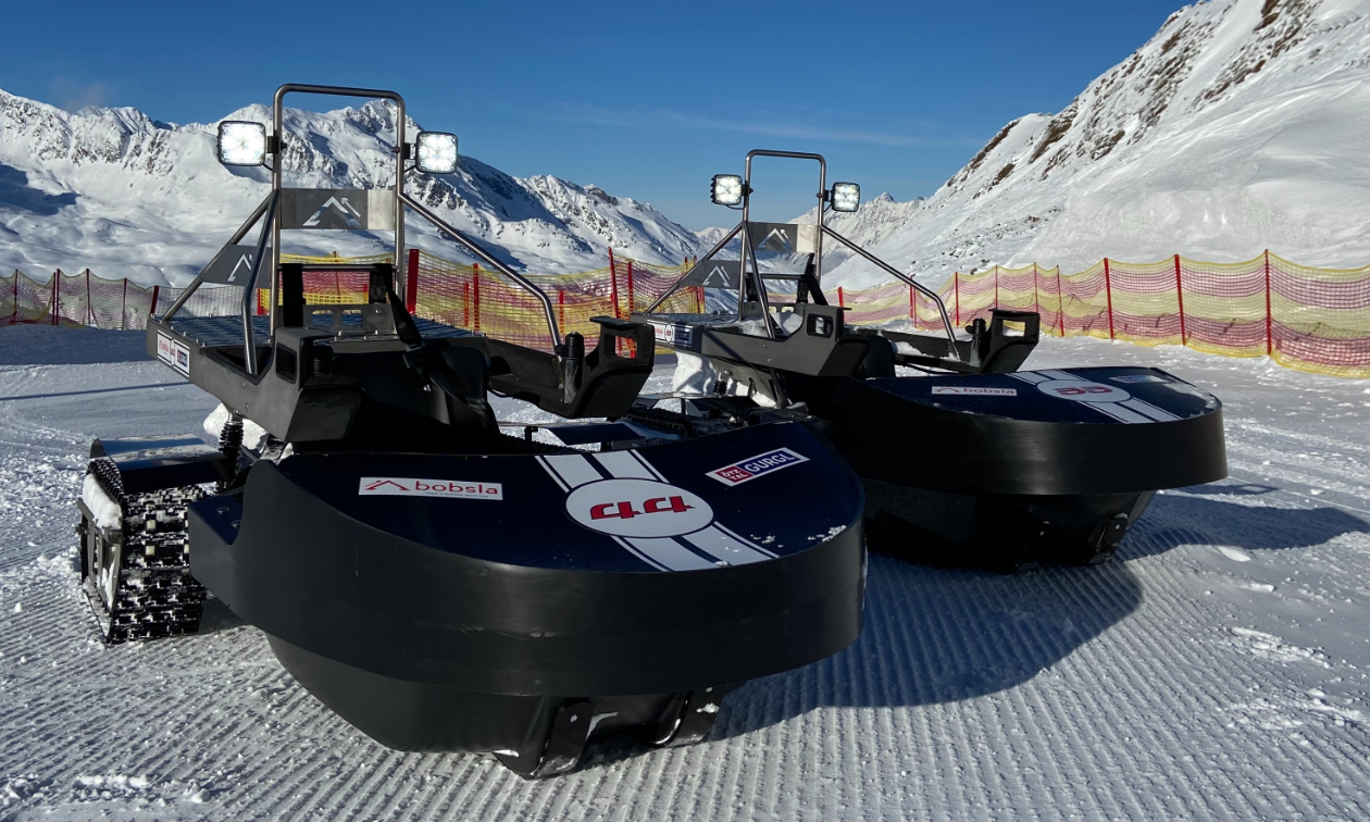 Two black Bobsla electric snowmobiles are parked next to each other on the snow. 