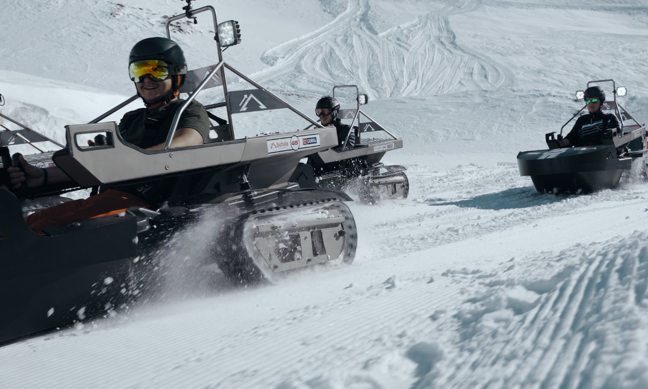 Three snowmobilers ride Bobsla electric snowmobiles on a race course. 