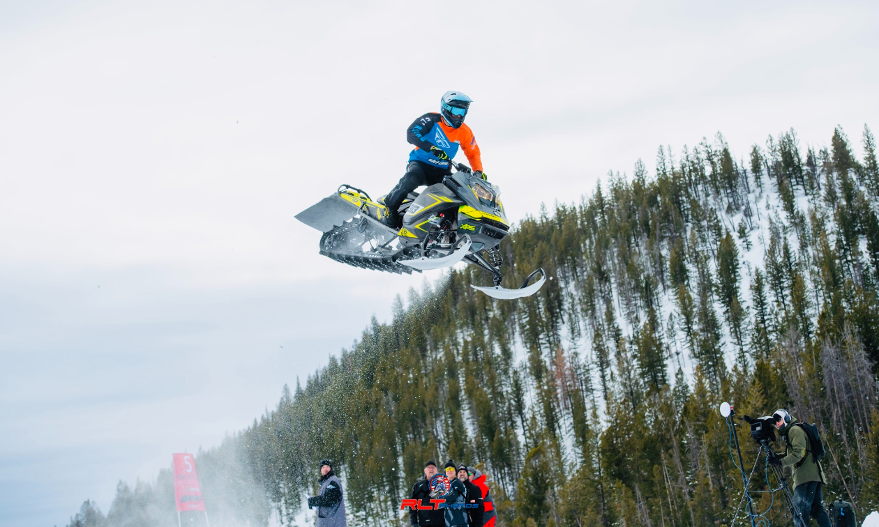 Brennan Mulvahill gets massive air from a jump over photographers on his yellow and grey Ski-Doo snowmobile. 