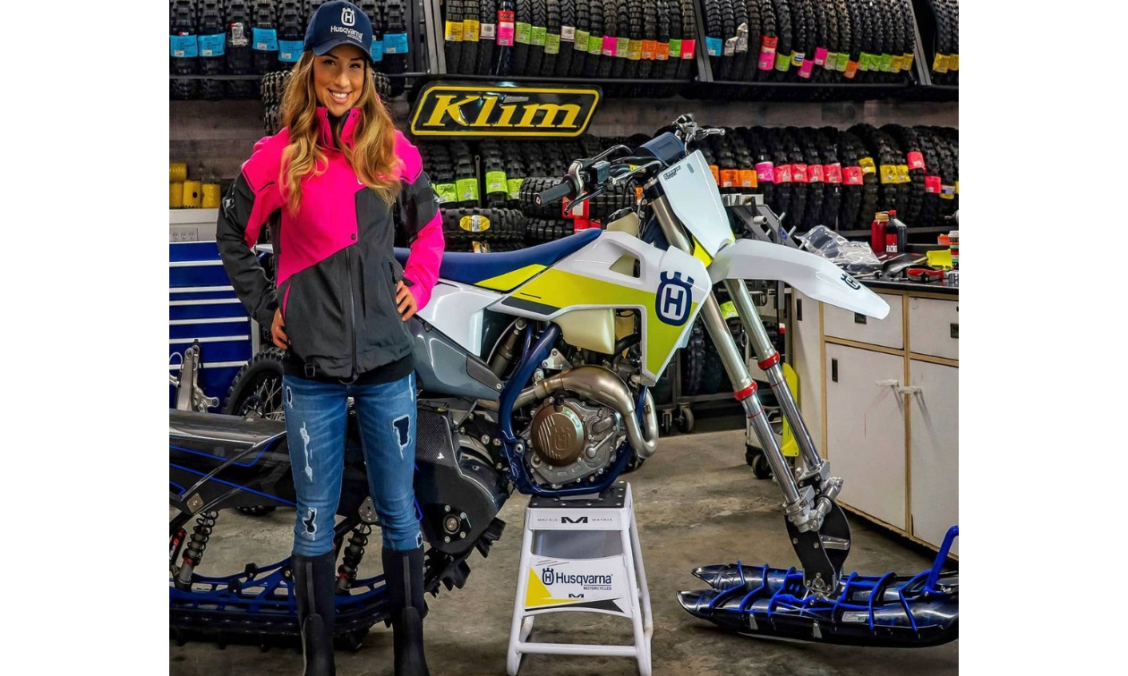 Cassandra Prochera stands next to her white and green Husqvarna FX 450 in a shop.