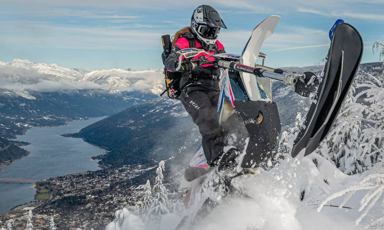 Cassandra Prochera gets a jump on her snow bike with Revelstoke and a lake at the base of the mountain. 