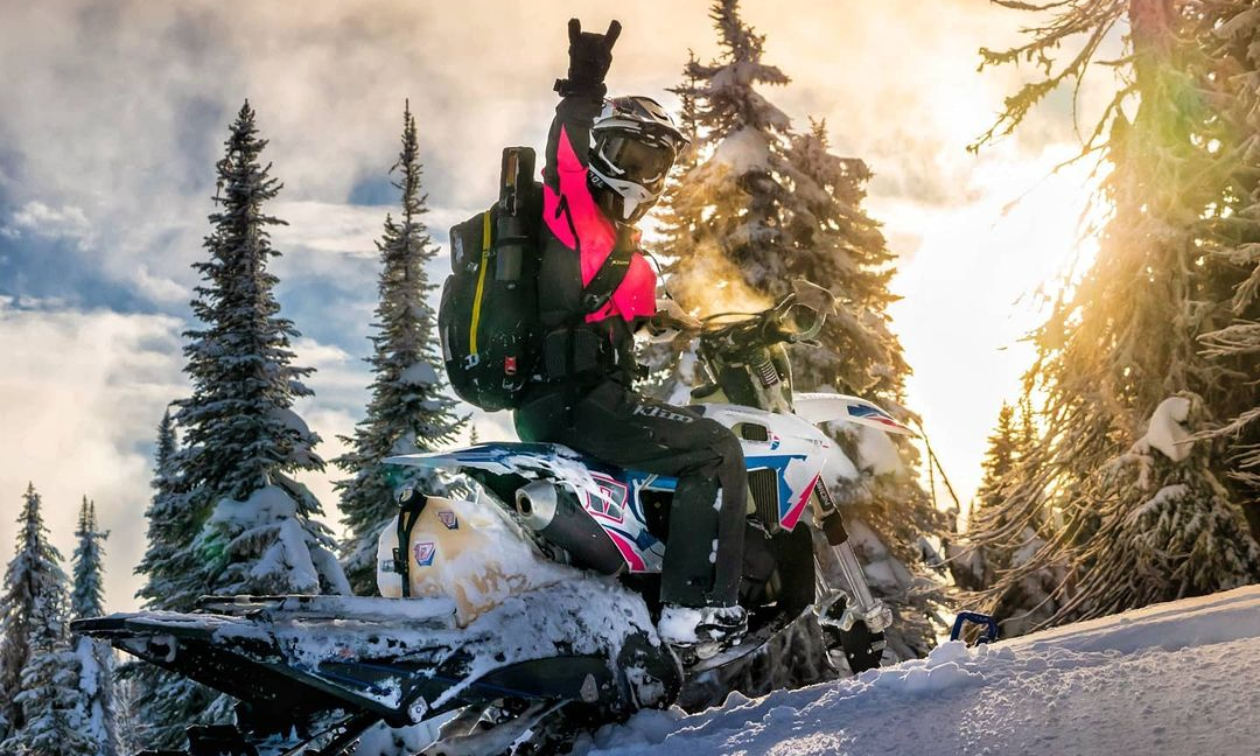 Cassandra Prochera throws up the devil horns from her snow bike as the sun dips below the snowy trees. 