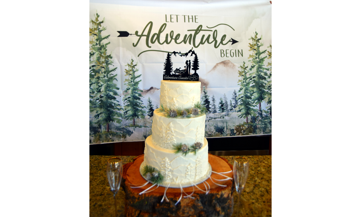 The cake was all white with mountains, pine trees, and capped with a black, silhouette cake topper with a snowmobile and a bride and groom that read Adventure Awaits.