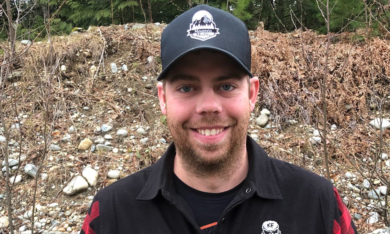 Colton Taphorn smiles, wearing a hat and a red and black long-sleeve shirt.