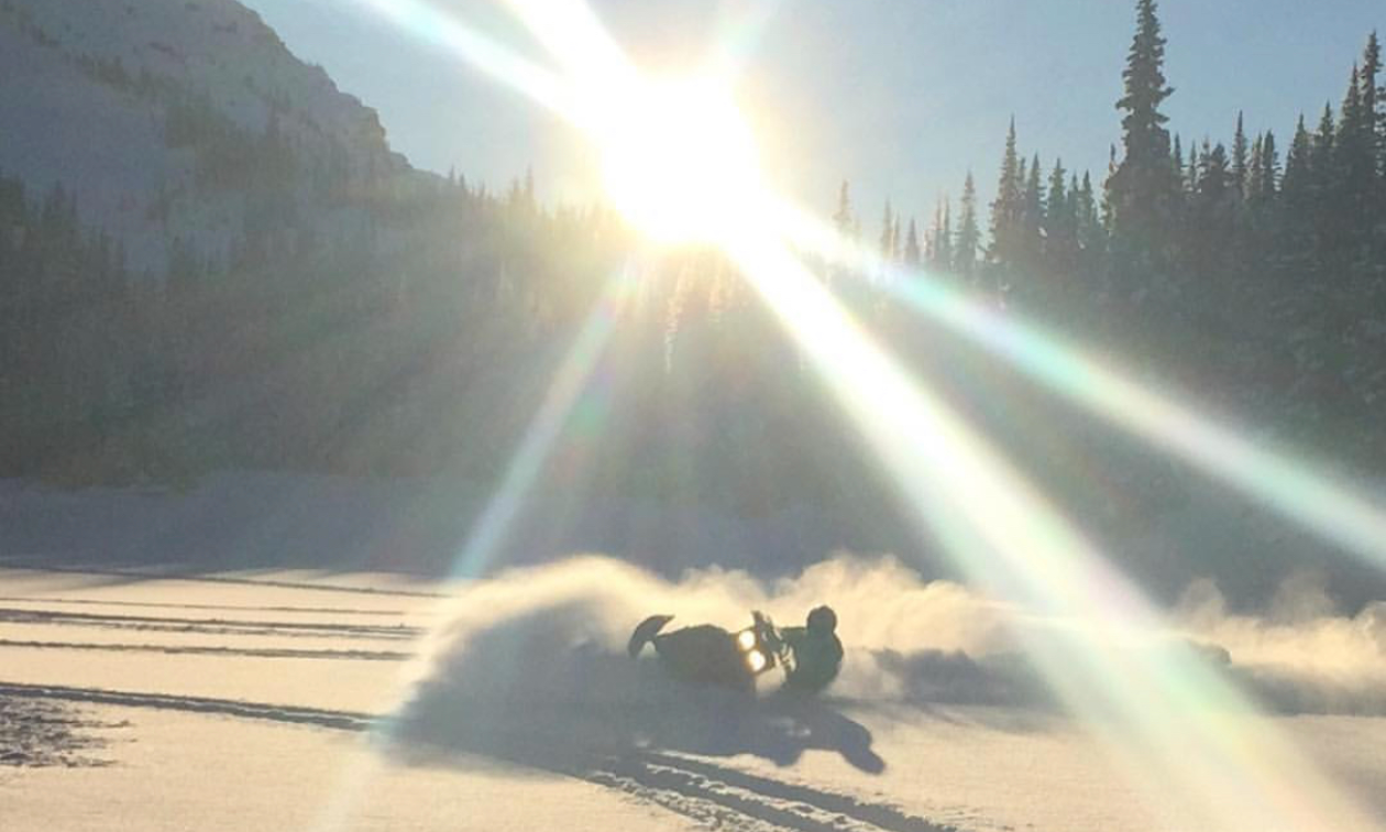 Colton Taphorn rides his snowmobile through deep powder snow while the sun shines bright overhead.