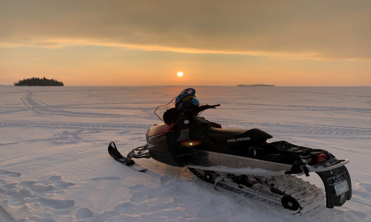 A red snowmobile is parked on a snowy field at dusk. 