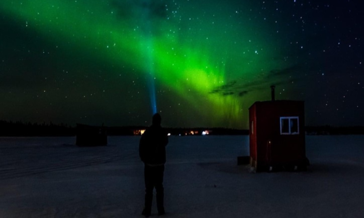 The northern lights shine bright green on a dark starry night.