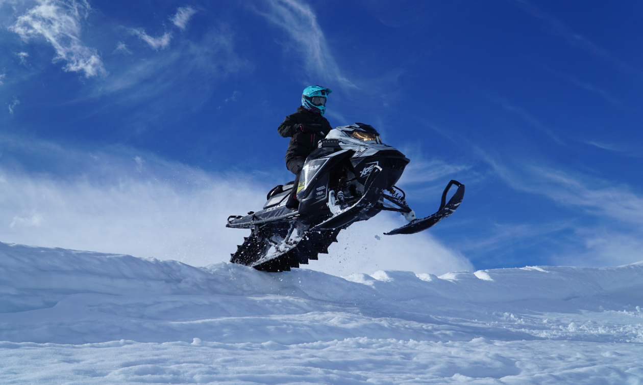 A snowmobiler gets air over a jump on a blue sky day.