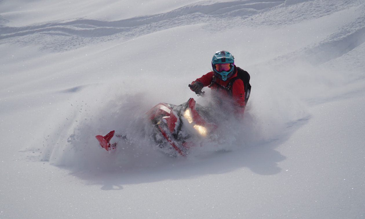 Genevieve Byl cuts into fresh powder snow on her red snowmobile. 