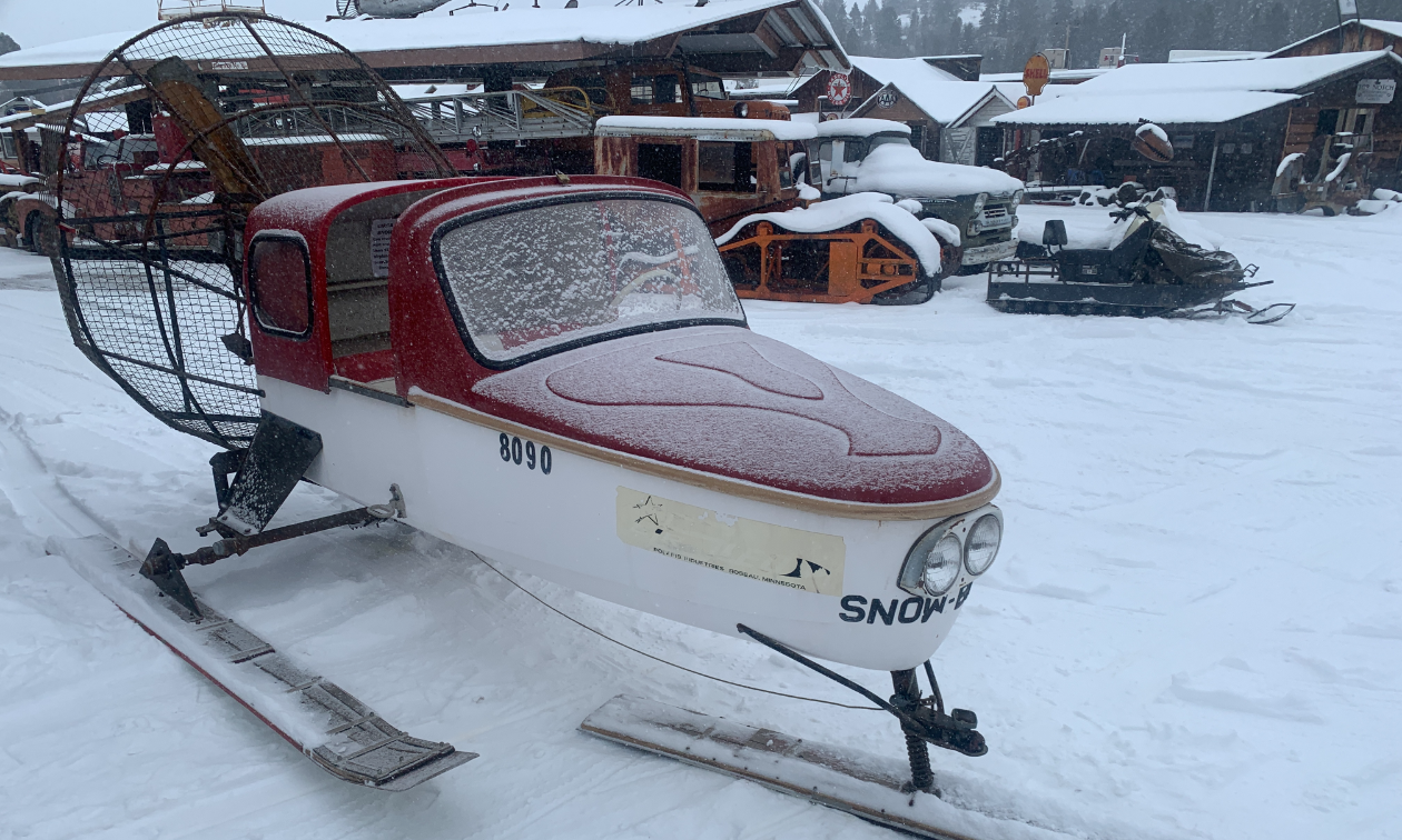 A snow plane is parked with a light dusting of snow covering its red hood. 