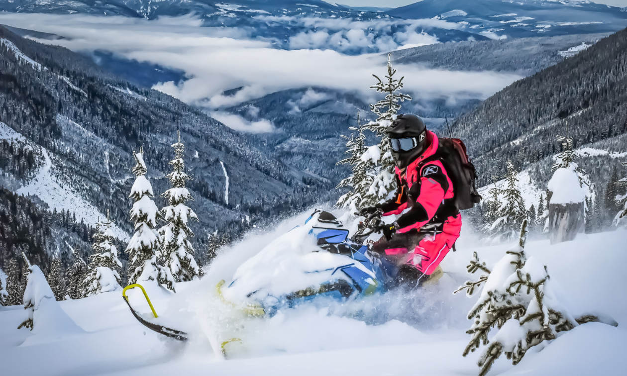 A snowmobiler in pink dashes through snow amidst mountains in British Columbia.