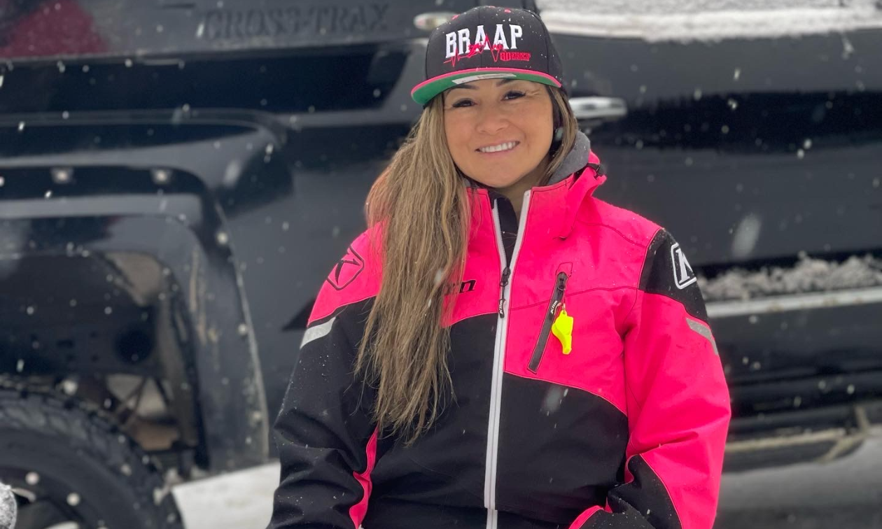 Jenny Hashimoto-Wiebe smiles in front of a black truck. She wears a pink and black jacket and a hat that says Braap.